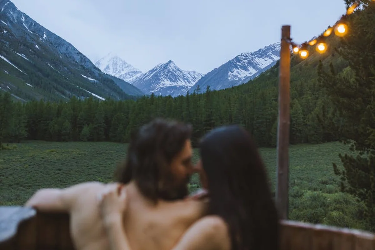 Smiling woman with a towel wrapped around her head, applying foamy face wash in a bathroom.