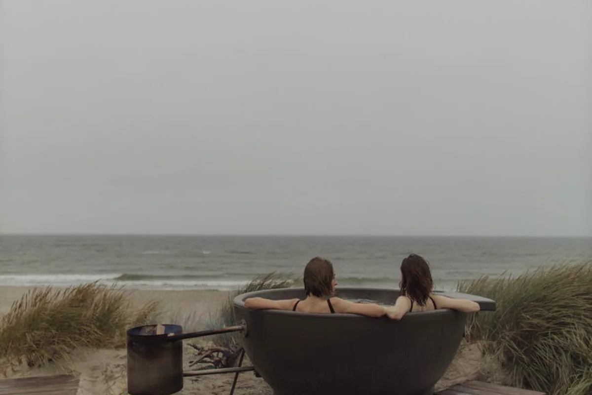Smiling woman with a towel wrapped around her head, applying foamy face wash in a bathroom.