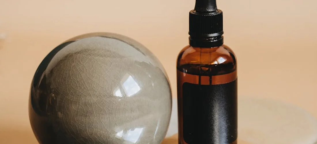 Essential oil bottle with a dropper next to a smooth round spa stone on a warm background.