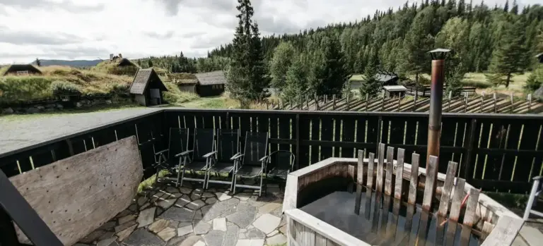 Outdoor balcony with a wooden hot tub and seating area, overlooking a scenic mountainous landscape.