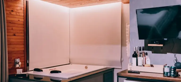 Indoor basement setup with a built-in hot tub, wood paneling, and a small bar area with bottles and a wall-mounted TV.