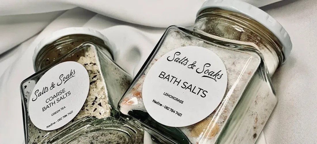Two glass jars labeled bath salts on a white fabric background, containing mineral salts for bath use.
