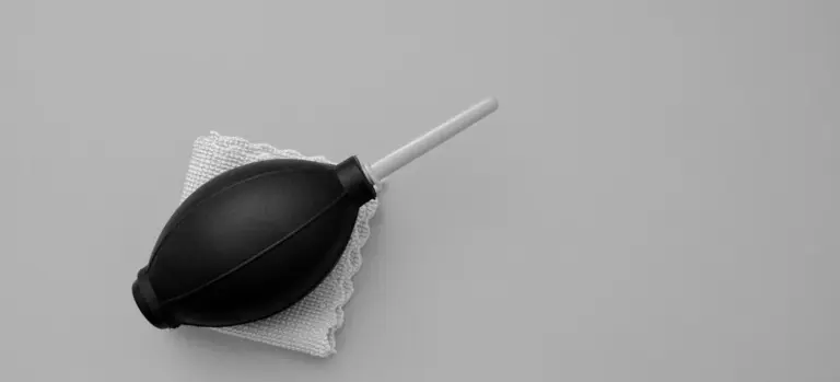 A black handheld air pump bulb with a long nozzle resting on a small white cloth on a gray surface.