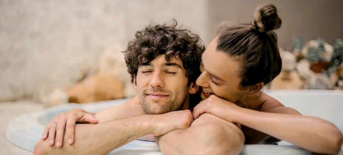 A couple relaxes in a hot tub, smiling with arms resting on the edge.