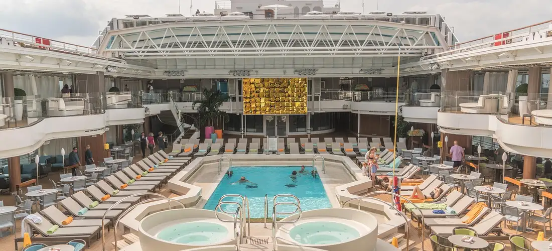 Cruise ship pool deck featuring two circular hot tubs in the foreground and lounge chairs surrounding the pool