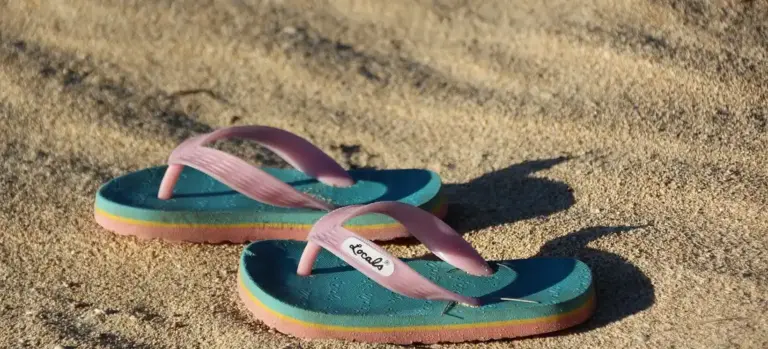 Colorful flip-flops with pink straps resting on a sandy surface