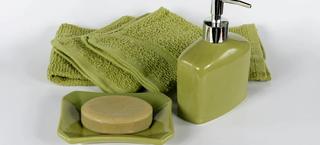 Green soap dispenser, matching soap dish with a bar of soap, and folded green towels arranged on a white surface.