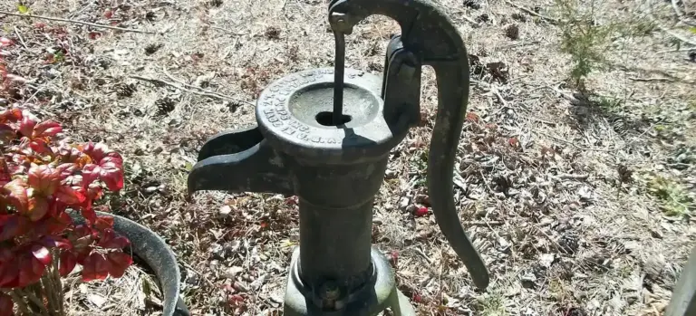 Old-fashioned manual water pump with a curved handle in a dry, rocky garden.