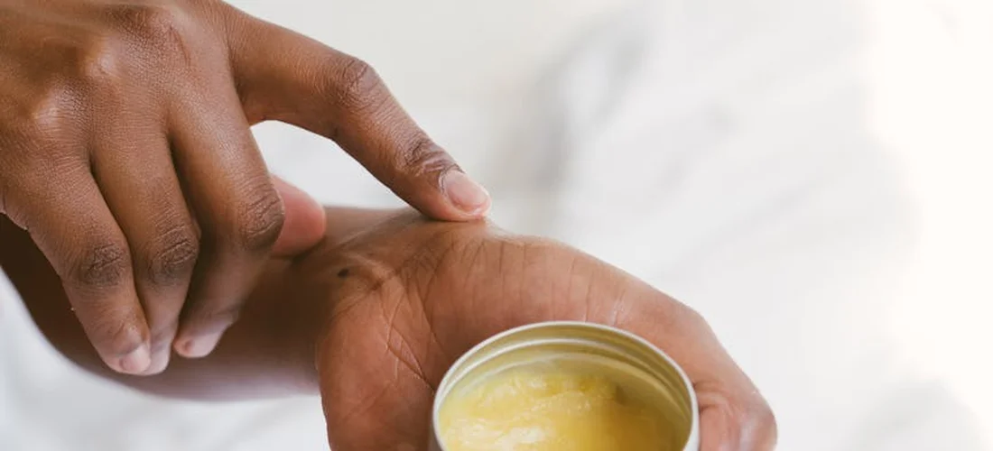 Close-up of a hand applying moisturizer from a small jar, suggesting post-wash hand care.