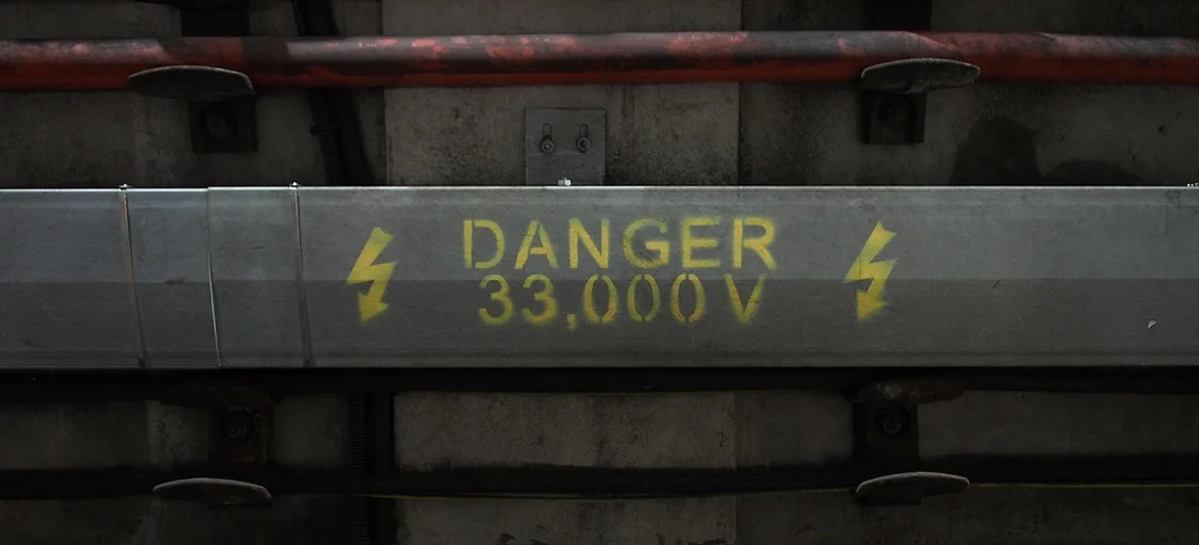 Close-up of a metal electrical conduit with a yellow 'DANGER 33,000 V' warning label