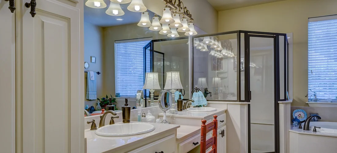 Bright bathroom interior with a double-sink vanity, mirrors, and a glass-enclosed shower.