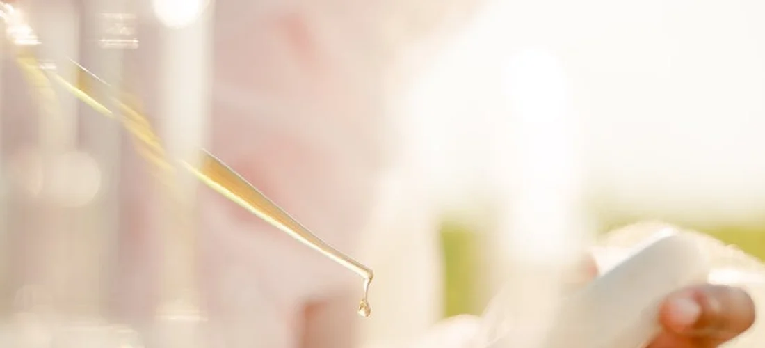 Close-up of a dropper releasing a drop of liquid with a soft, blurred background.