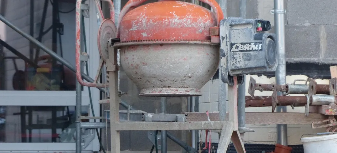 Portable concrete mixer on a construction site with scaffolding, illustrating base work for a hot tub installation.