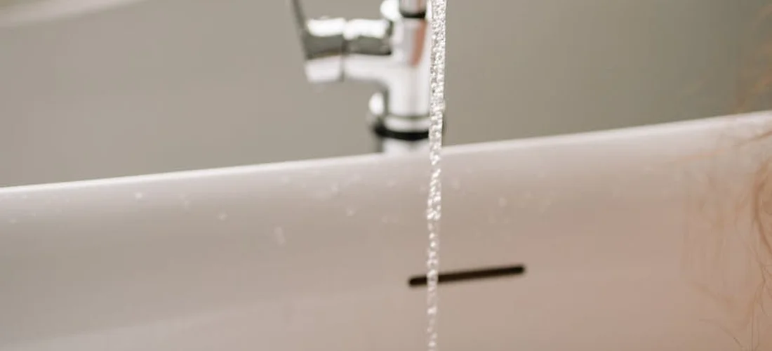 Close-up of a faucet pouring water into a white bathtub, illustrating the maintenance focus for clean, consistent hot-tub bubbles.