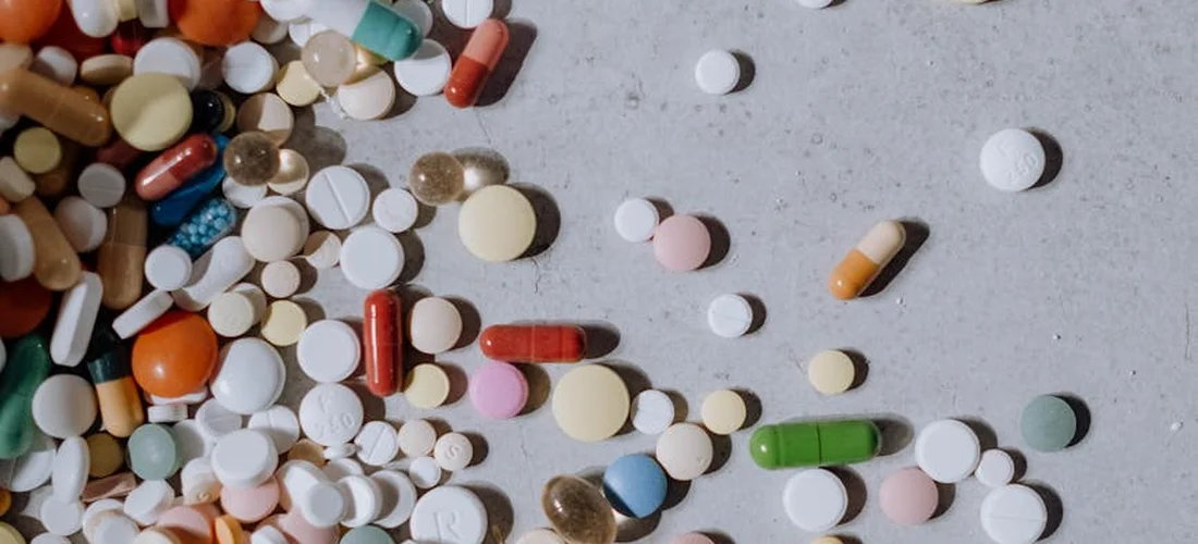 A spread of assorted pills, tablets, and capsules on a light surface, representing the chemicals used for hot tub maintenance.