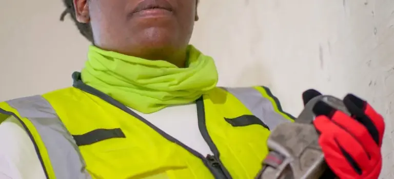 Close-up of a maintenance worker wearing a neon yellow safety vest and red gloves, holding a tool.