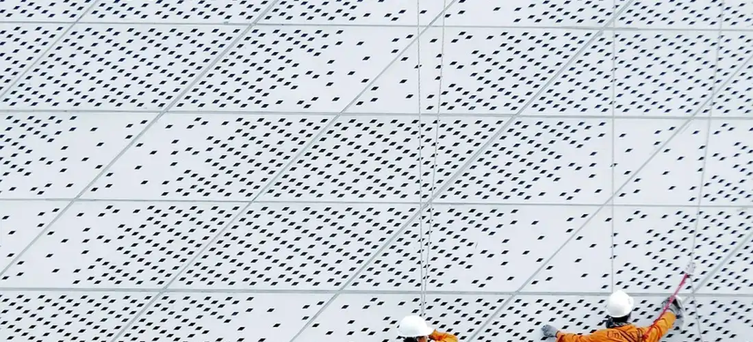 Worker wearing orange safety gear on a perforated metal platform, partially visible