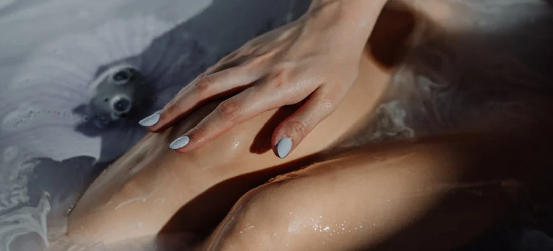 Close-up of a person relaxing in a hot tub with steam and bubbles, a hand resting on their upper arm.