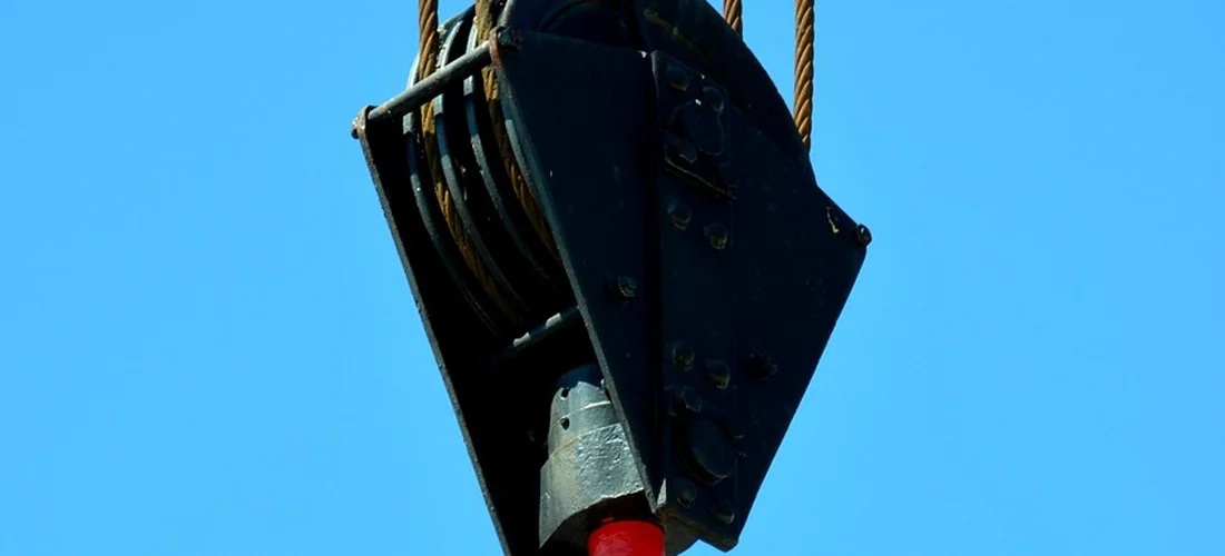 Close-up of a hot tub cover lifter mechanism suspended by ropes against a clear blue sky.