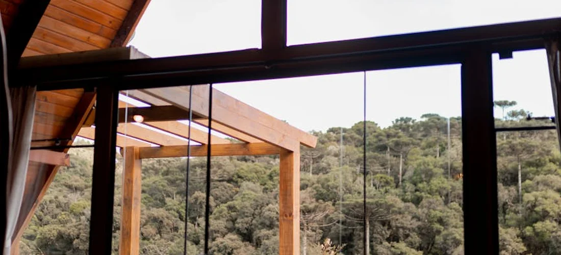 Interior view through large glass doors of a wooden deck with timber beams and a forest backdrop, highlighting durable outdoor construction.