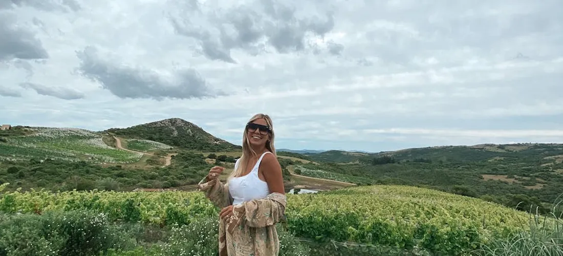 A woman standing in a green, hilly landscape holding a small dog.