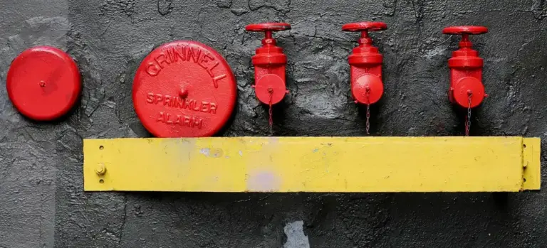Close-up of red plumbing valves mounted on a dark textured wall with a yellow bar beneath