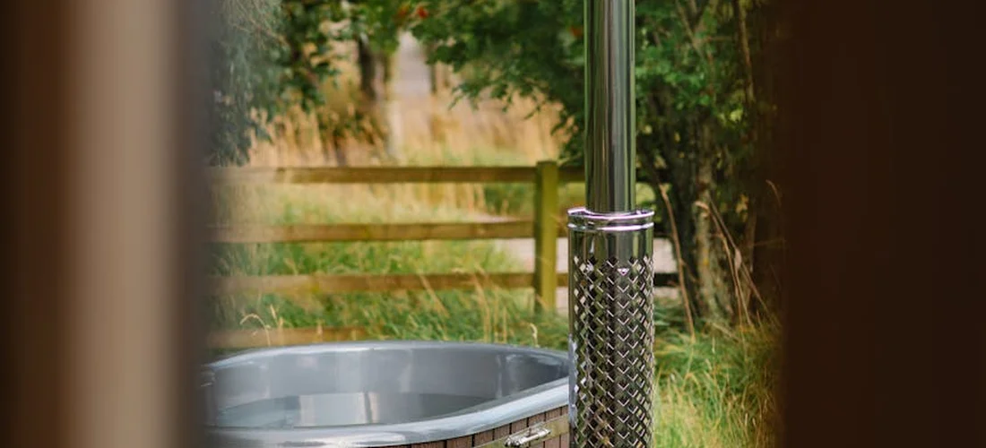 Outdoor hot tub in a backyard, viewed from a doorway, with a wooden fence and greenery in the background.
