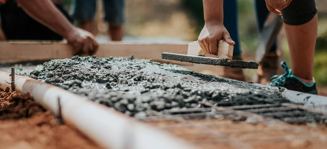 Hands smoothing a freshly poured concrete foundation pad with a trowel during hot tub installation.
