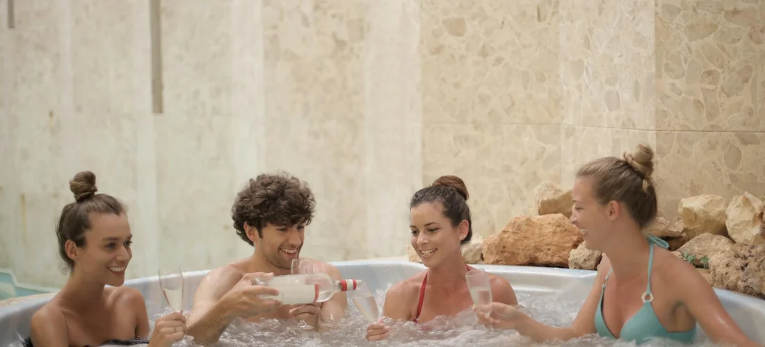 Four people relaxing in an indoor hot tub with stone walls, highlighting moisture and ventilation considerations.