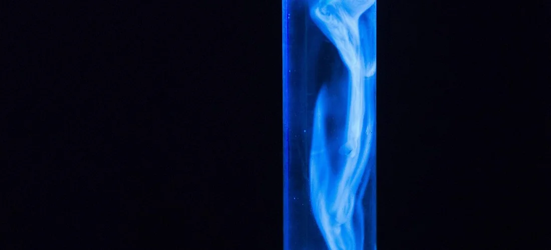 Blue-lit vertical tube with wisps of vapor against a dark background, symbolizing chemical activation in hot tub water treatment.