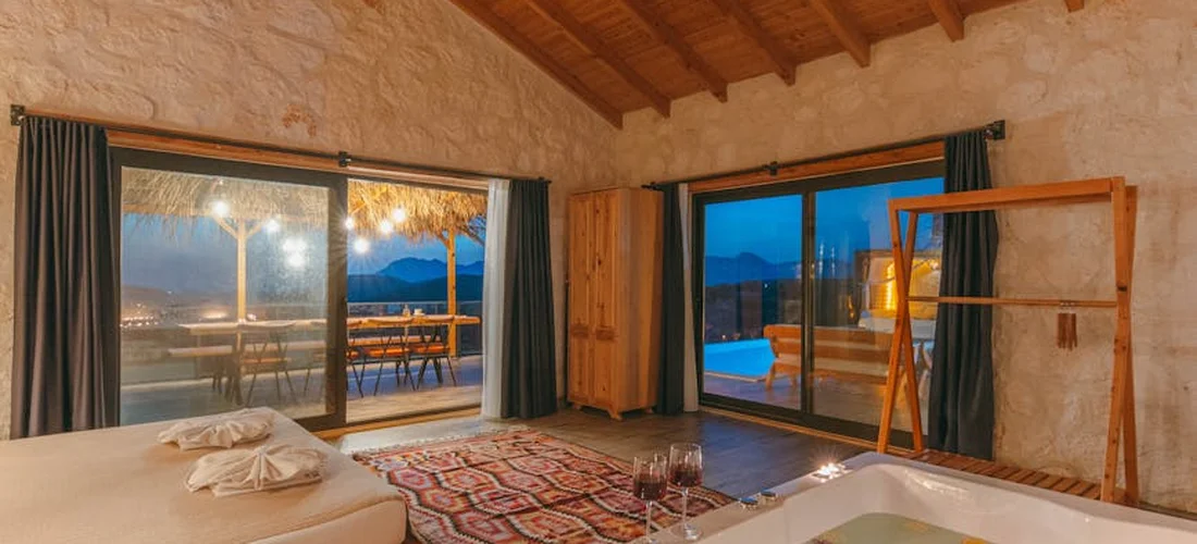 A rustic, sunlit spa room with a built-in hot tub beside large sliding glass doors opening to an outdoor pool.