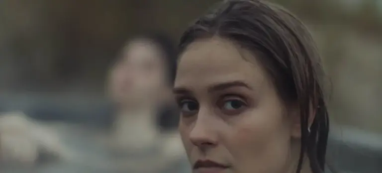 Close-up of a woman with wet hair, standing near a blurred hot tub in the background.