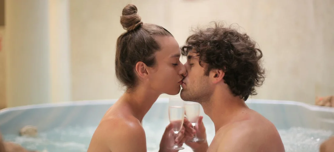 Couple kissing in a home hot tub while toasting with champagne glasses.