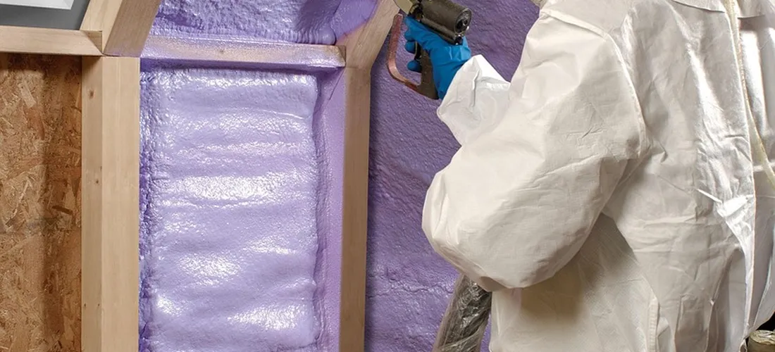 Worker in protective suit installing purple foam insulation in a hot tub wall