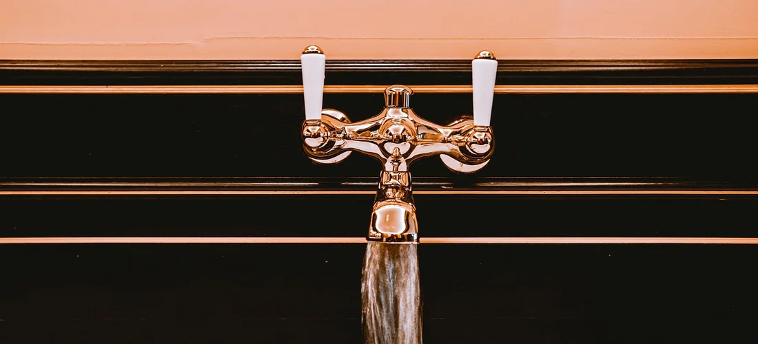 Close-up of a shiny faucet with running water against a dark background