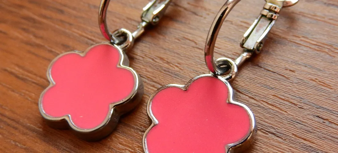 Two pink flower-shaped jewelry charms with silver metal clasps on a wooden surface