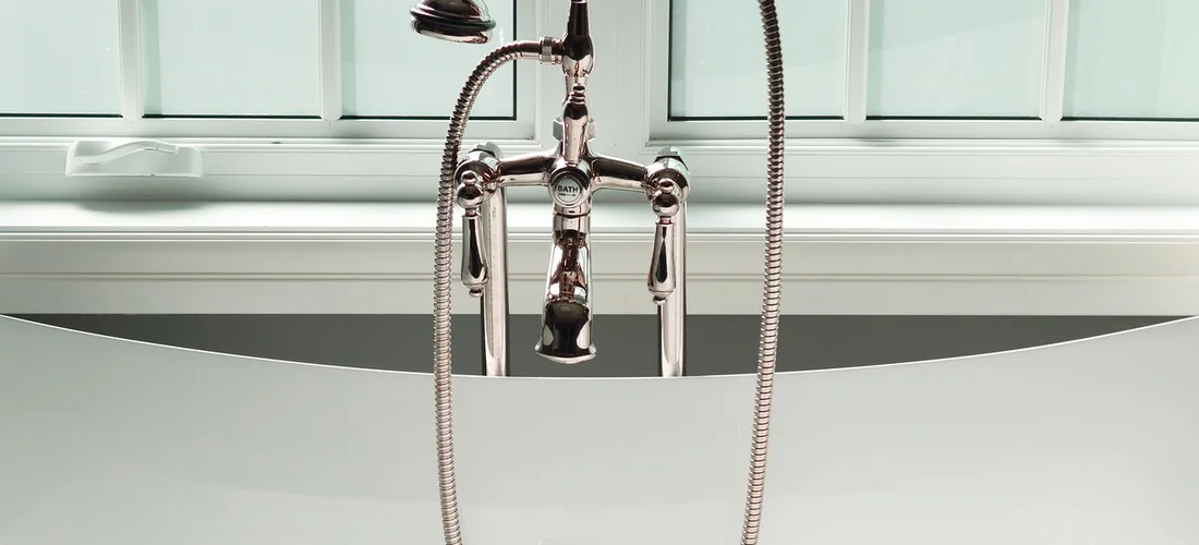 Close-up of a chrome hot tub faucet with dual handles and a handheld shower hose, reflecting light.