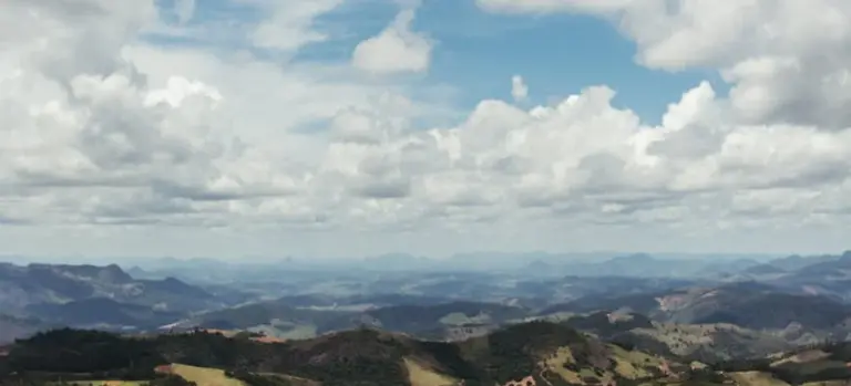 Panoramic landscape of rolling hills and distant mountains under a partly cloudy sky.