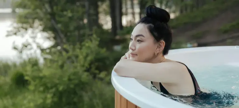 Person leaning on the edge of an outdoor hot tub surrounded by green foliage