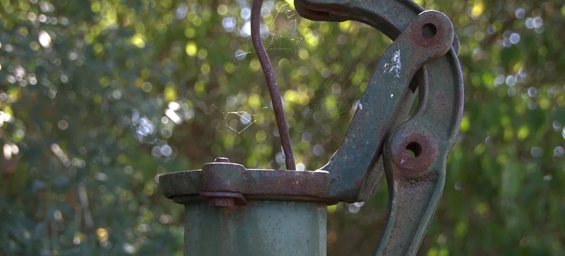 Close-up of a rusted metal hot tub pump component outdoors, showing a bracket and lever