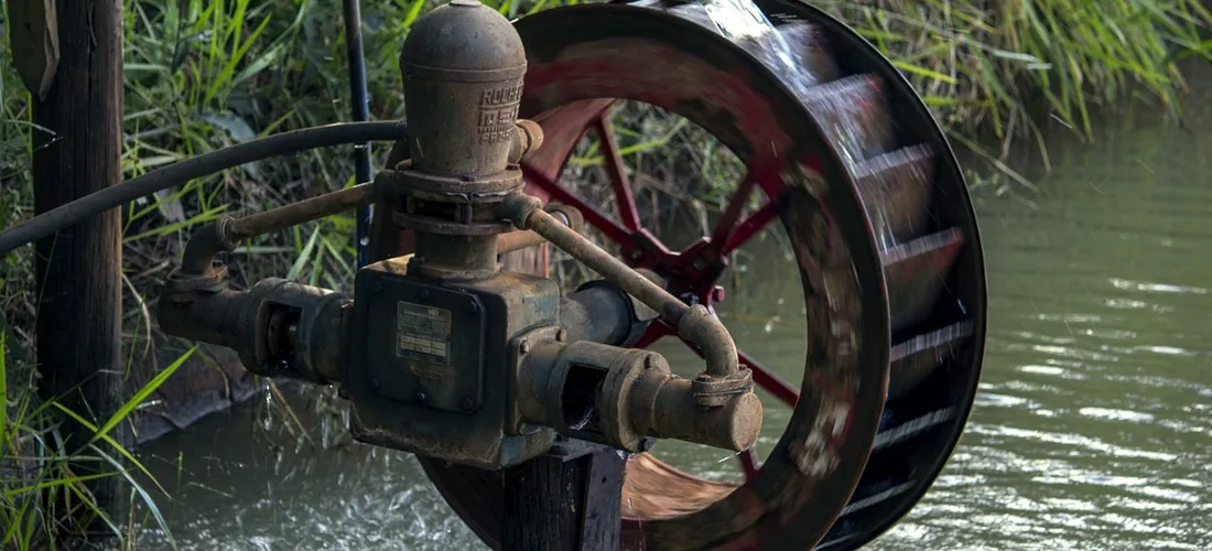 Close-up of a mechanical water pump wheel with piping and a valve, illustrating pump priming for hot tub systems.