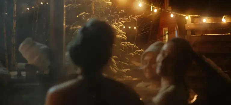 People relaxing around an outdoor hot tub at night under string lights.