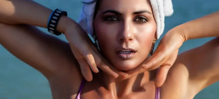 Close-up portrait of a woman wearing a swimsuit with a towel wrapped around her head, posing near water.