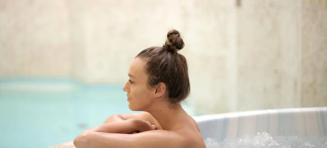 Person with hair in a bun relaxing in a hot tub, preparing to address common water issues
