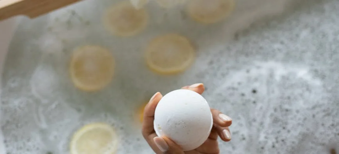 A hand holds a white bath bomb above a bubbling hot tub