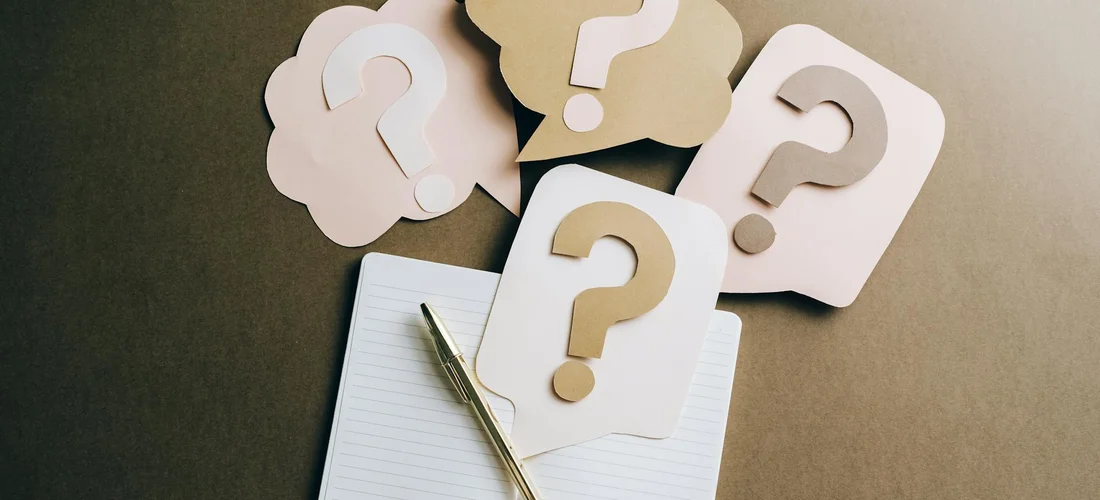 Close-up of question-mark cards around a notebook and a pen on a dark surface, symbolizing questions about hot tub water chemistry costs.