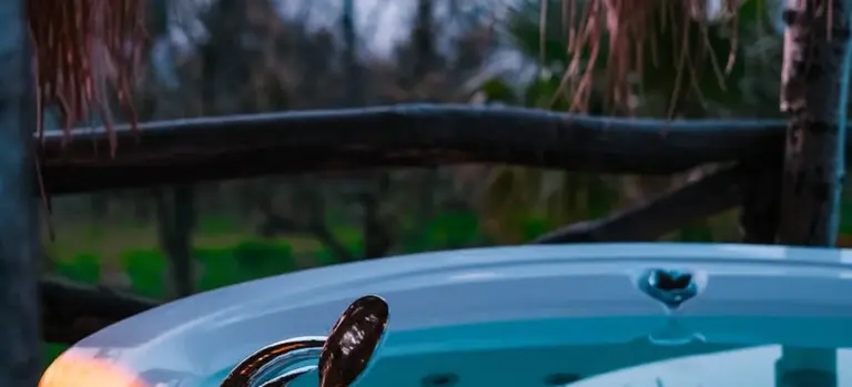 Close-up of a blue hot tub with water near the rim, a metal handle in the foreground, and a blurred outdoor background.