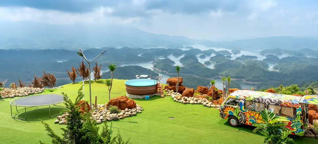 Outdoor resort scene with round hot tubs on a grassy hill, a colorful van, and a scenic mountainous backdrop.