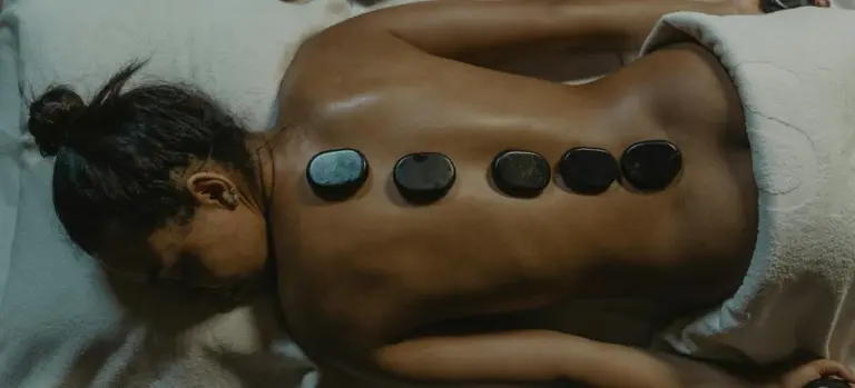 Person lying face down on a massage table with smooth hot stones placed along the spine