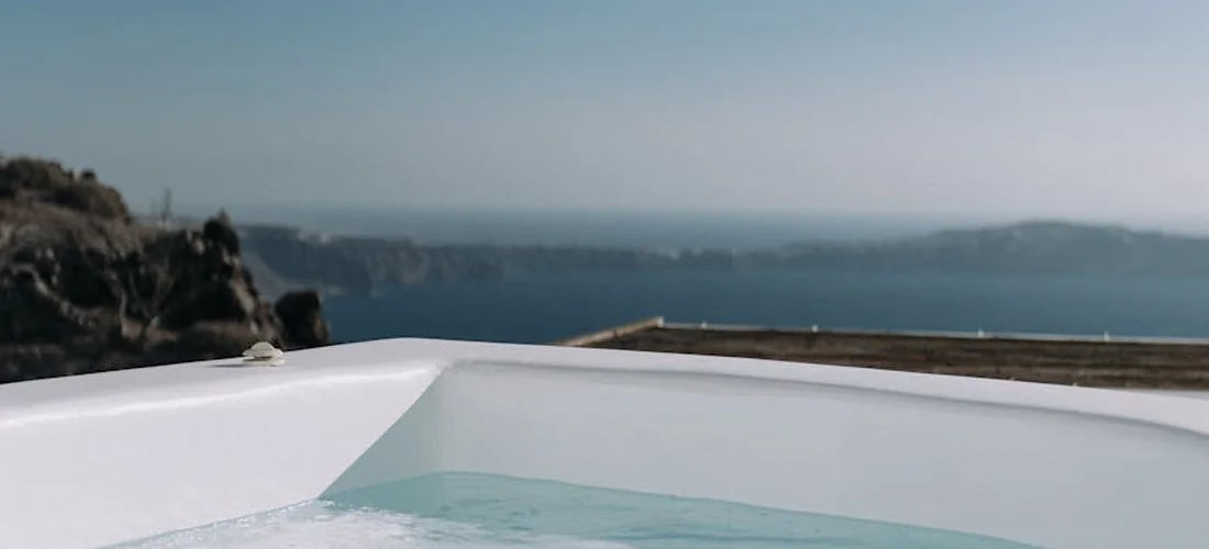 White hot tub edge with clear water, set against a calm seaside landscape.